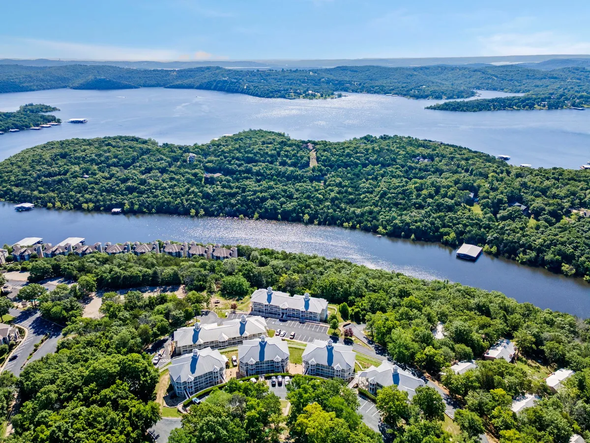 The hero image showcases a serene view of Table Rock Lake framed by lush tree coverage and surrounding Ozark hills, with the soft glow of sunset reflecting off the tranquil water. Residential buildings of the resort peek through the greenery, suggesting a peaceful lakeside retreat. The scene hints at opportunities for boating, fishing, hiking, and wildlife spotting, all amid natural beauty.