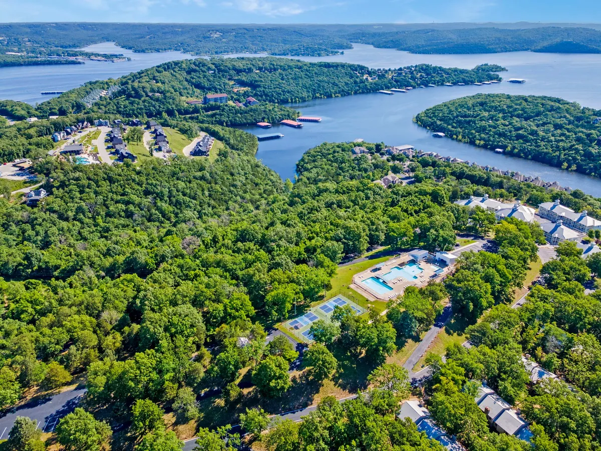 A panoramic vista showing Table Rock Lake, swimming pool area, tennis courts, and residential buildings nestled within rolling green hills. The image captures both water- and land-based recreational amenities in one cohesive scene.