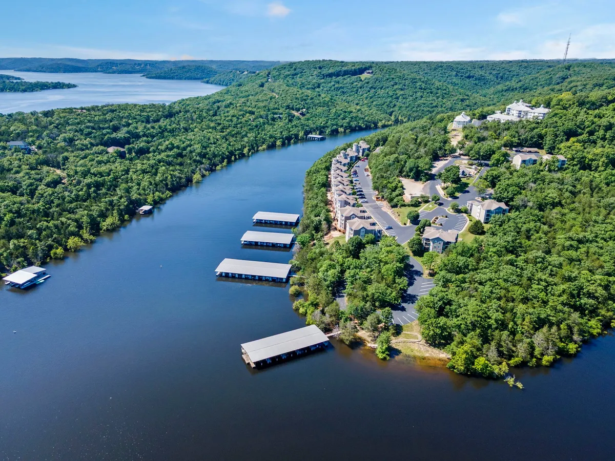A broad view of the river, marinas, surrounding hills, and residential buildings, with visible walking trails along the water. The landscape is serene, signaling opportunities for lakeside walks and exploration.