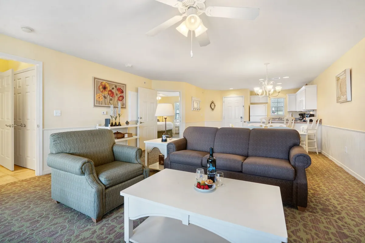 A comfortable living room area featuring a sofa, armchair, coffee table, and decorative wall art. The space is well-lit, casual, and inviting, perfect for relaxing with family or spending time with your pet indoors.