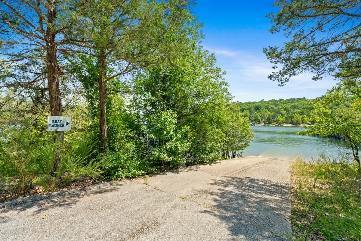 A clear view of the boat launch area, marked by a prominent sign, with a concrete ramp leading to the water and surrounded by greenery. The distant water offers a glimpse of lake activities like boating and fishing.