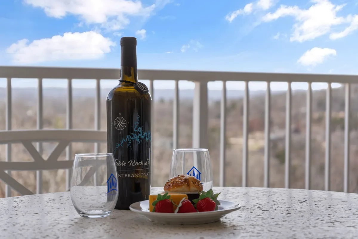 An exterior balcony or deck set for dining with a wine bottle, glasses, and a plate of food, all overlooking a tranquil, green view. The setting suggests peaceful outdoor moments and direct access to fresh air from the condo.