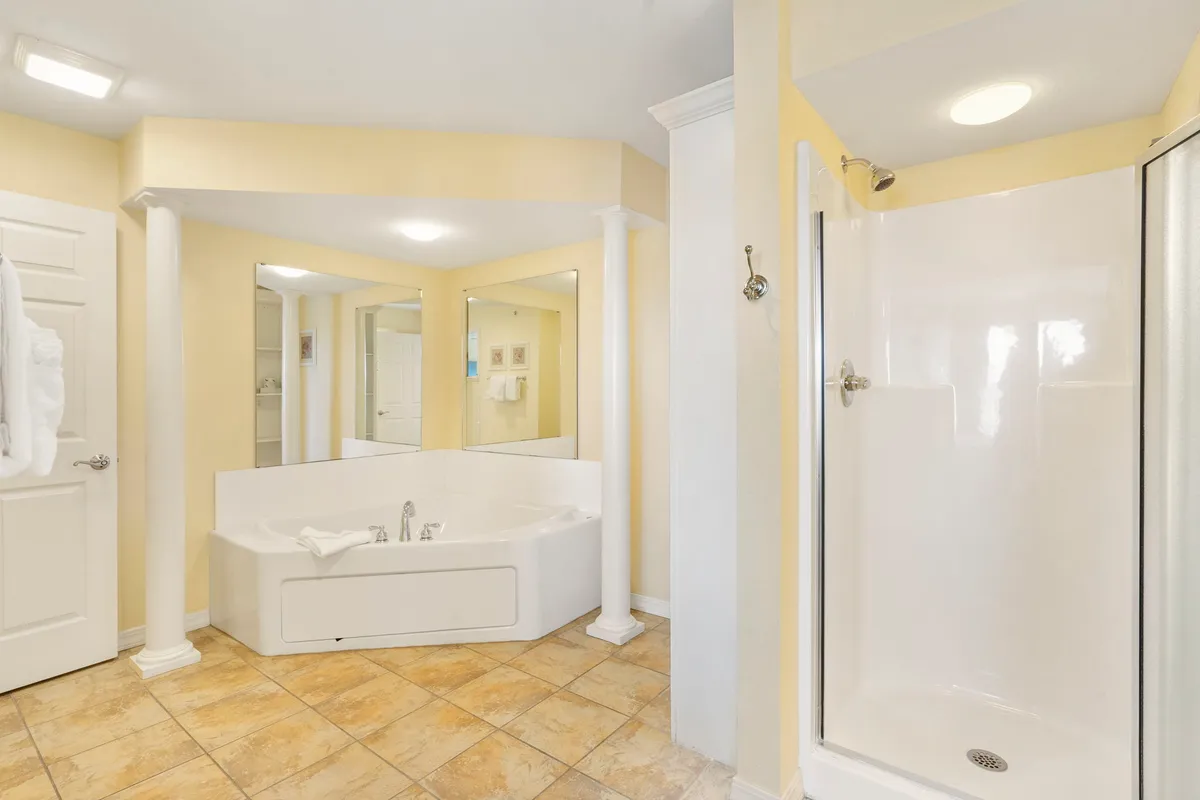 A luxurious ensuite bathroom featuring a deep soaker tub, elegant shower, and expansive mirrors set between graceful columns. The space is tranquil and designed to encourage rejuvenation and indulgent self-care.