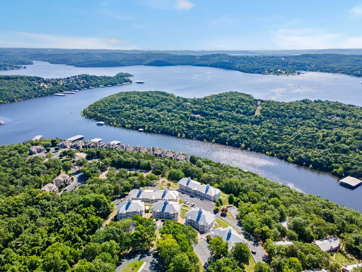A tranquil view of Table Rock Lake surrounded by lush, green hills and residential buildings in the distance. The serene water invites boating, fishing, and lakeside relaxation, while the untouched greenery hints at hiking and nature walks nearby.